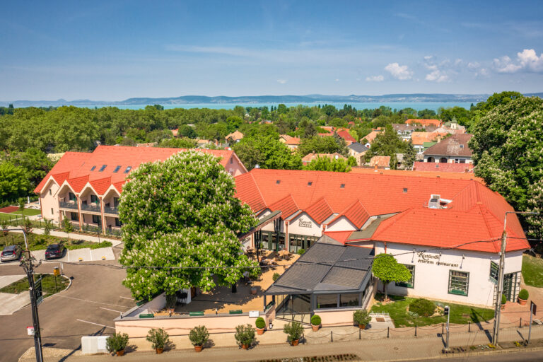 Außenansicht des Kistücsök Food & Room mit rotem Ziegeldach, begrüntem Innenhof und Blick auf den Balaton im Hintergrund.