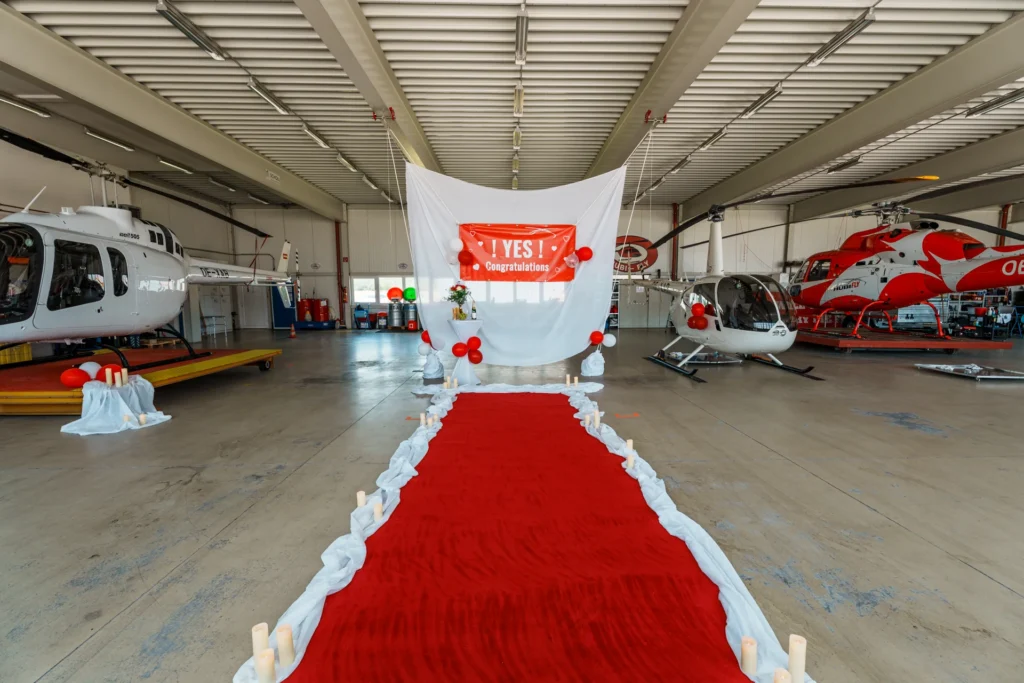 Aufbau in einem Hubschrauber Hangar. Roter Teppich vor einem weißen Vorhang. Stehtische mit Getränke und Blumen.