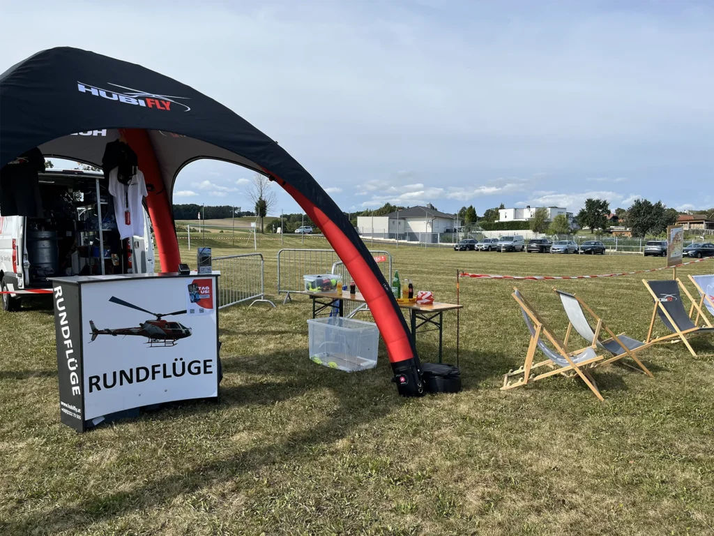 Mobiles Setup für Hubschrauberrundflüge mit kleinem Zelt und Liegestühle auf einer großen Wiese platziert.