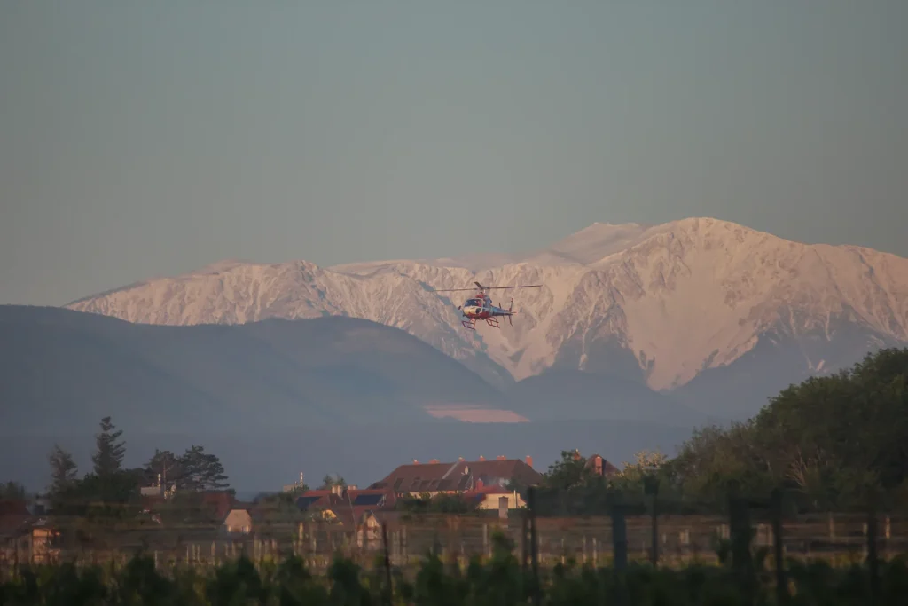 Hubschrauber fliegt über Weinfelder. Im Hintergrund Schneebedeckter Berg