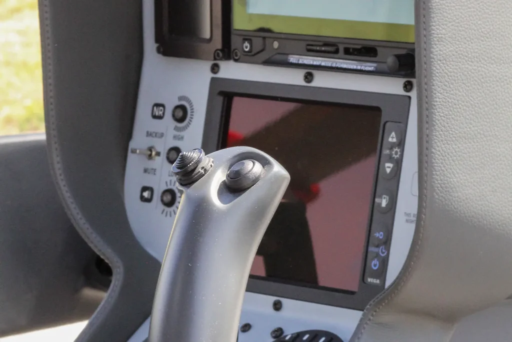 Close-up of an aircraft joystick in front of a flight display panel in the cockpit