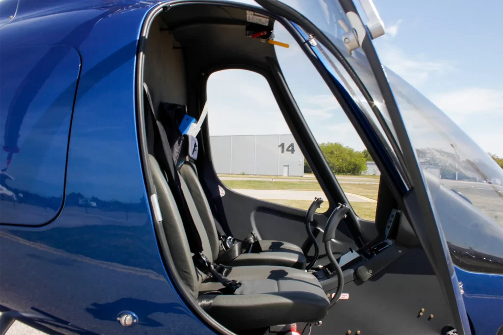 Open blue helicopter cabin door showing cockpit with seats and controls, runway and a building with '14' in the background.