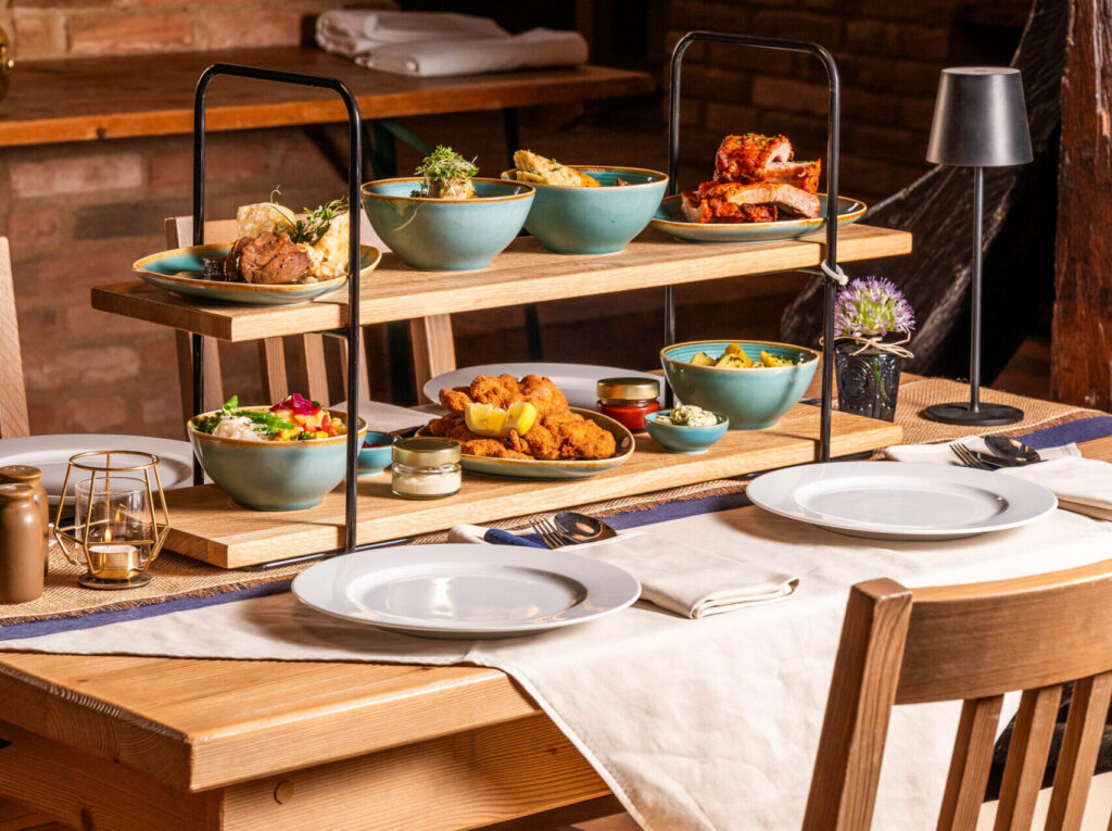 Two-tier wooden serving tray with turquoise bowls of food on a rustic dining table.